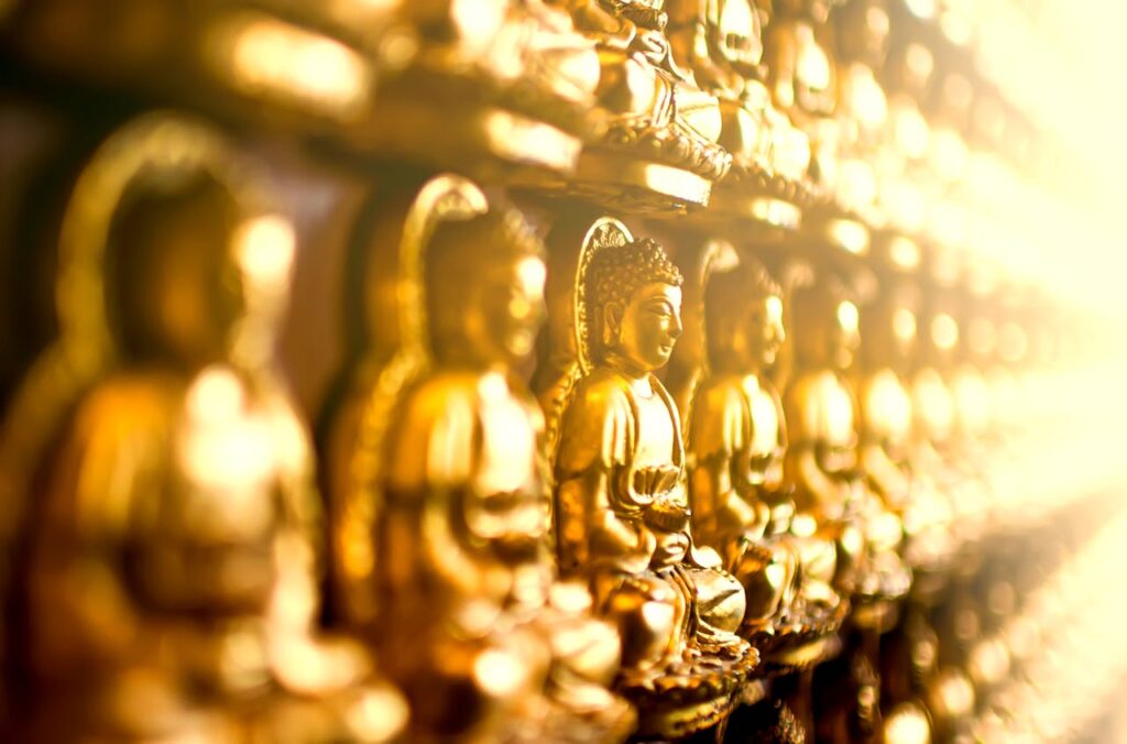 Row of golden Buddha statues in soft focus, symbolizing worship and spirituality in a sacred setting.
